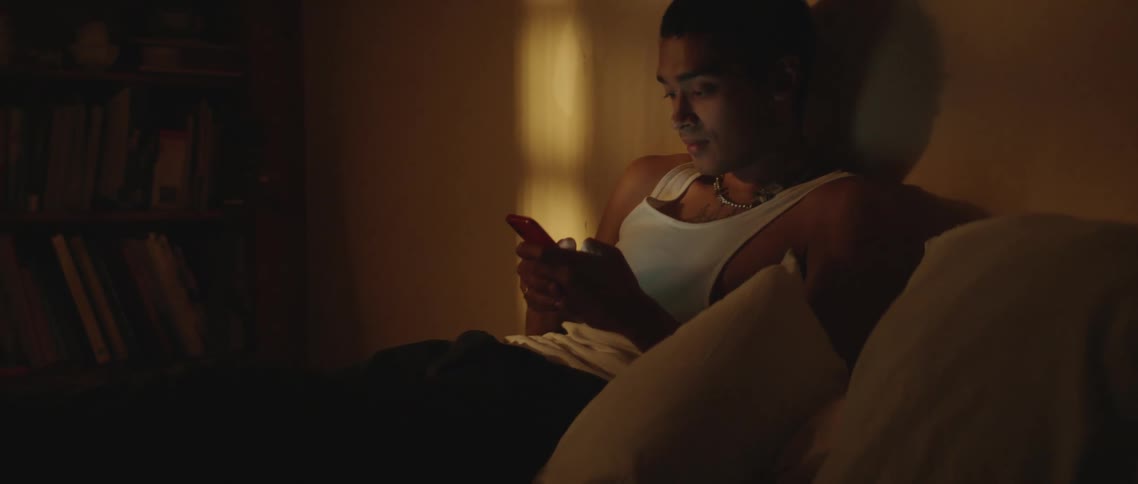 A man is lying on a bad and is seems to be texting on his smartphone