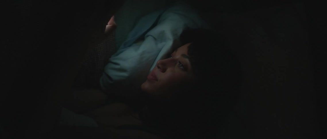 Woman lying down in dark room is lit by light from mobile phone screen