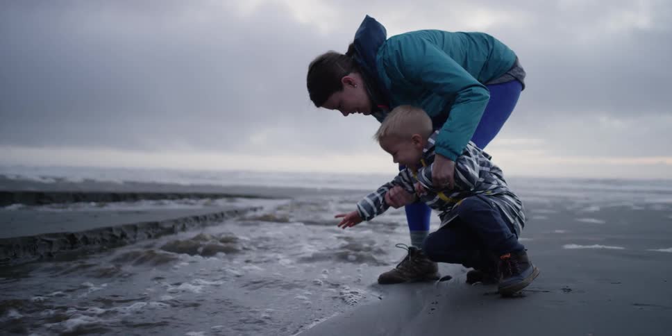 A woman holds a child as he moves his hands in the water