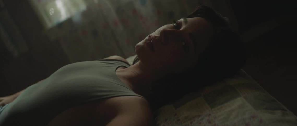 A young woman lays on her back on a bed and then slowly looks at the camera