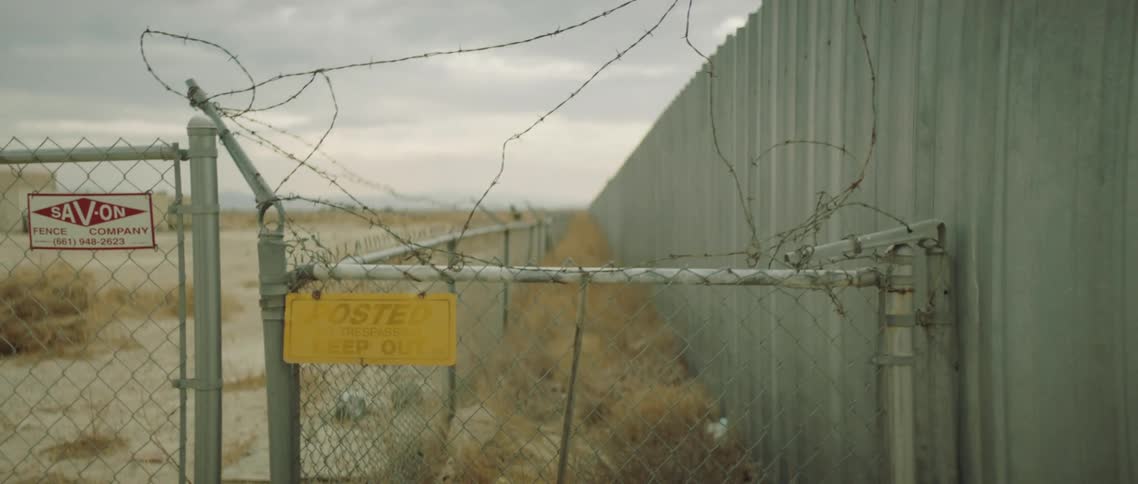 Long building surrounded by a chain link fence with barbed wire across the top