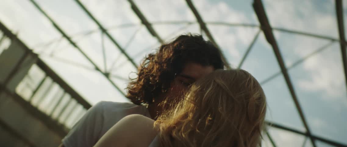 A man and woman stand with their faces together in the ruins of a building during the day