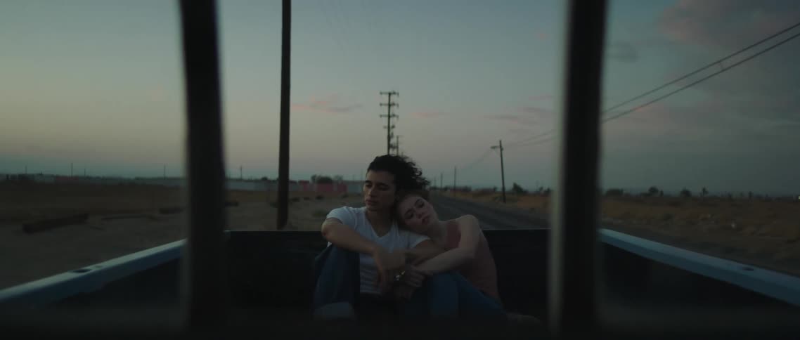 A young couple sit close together as they ride in the back of a pickup truck