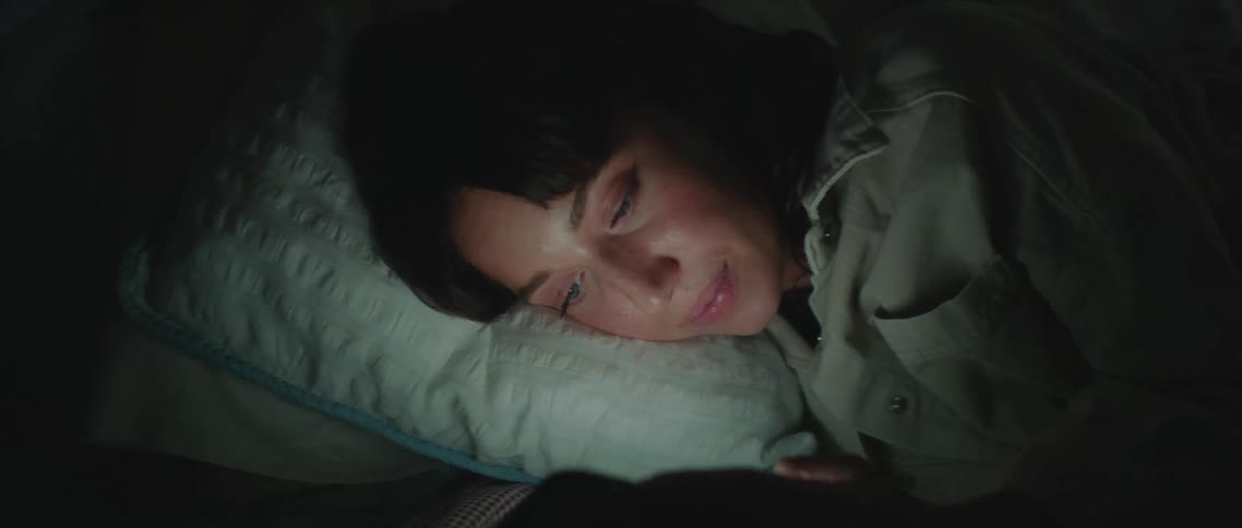 A woman is lying on a bed and texting on her smartphone