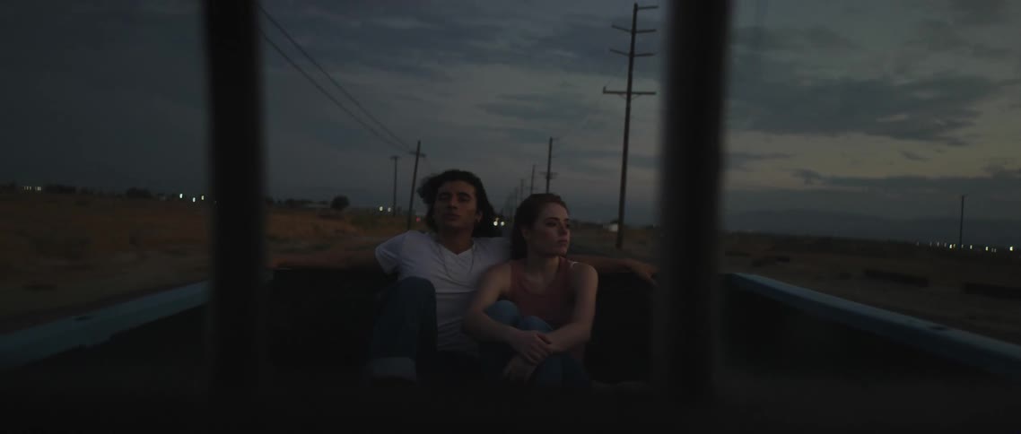 Young couple riding on the back of a truck driving on a rural road at evening