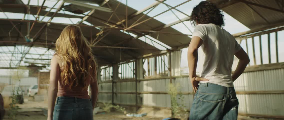 Man and woman walk through ruined building containing abandoned cars