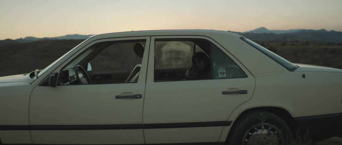 A man and a woman in the back seat of a vehicle with a landscape the sky and clouds in the background