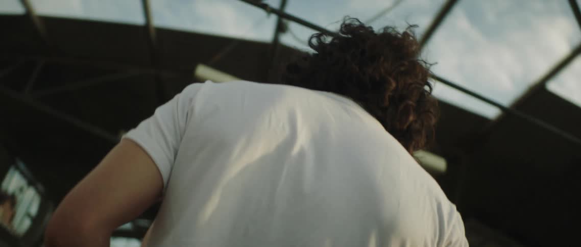 A man and woman stand in an unfinished building kissing and embracing while the sun shines down on them