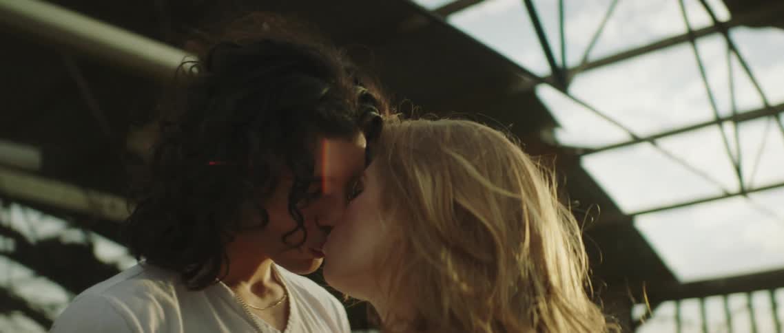 A kissing couple standing outside in the sunshine with beams above them