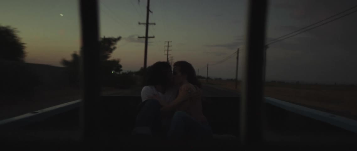 Young couple kissing while sitting on the back of a moving car driving on a rural road at sunset