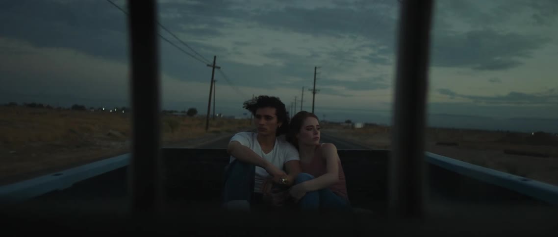 A couple are riding in the back of the pickup truck at sunset