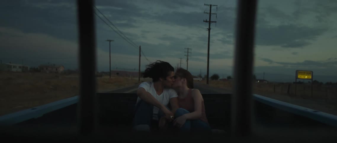 A man and a woman riding in the back of the pickup truck kissing with sky and clouds in the background