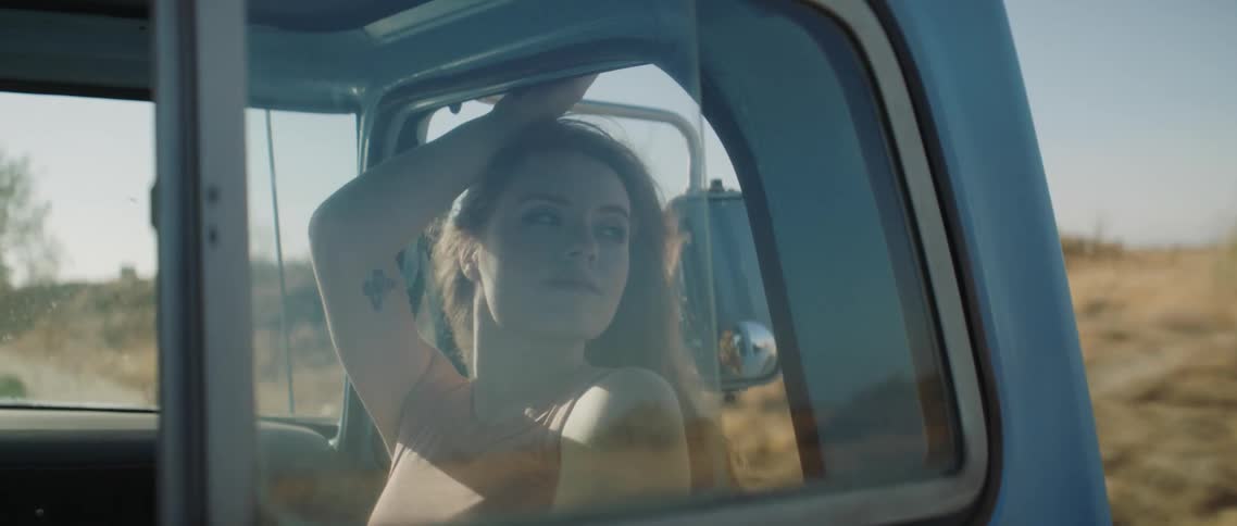 A teenager girl sits in a truck and leans her head out the window as it drives along