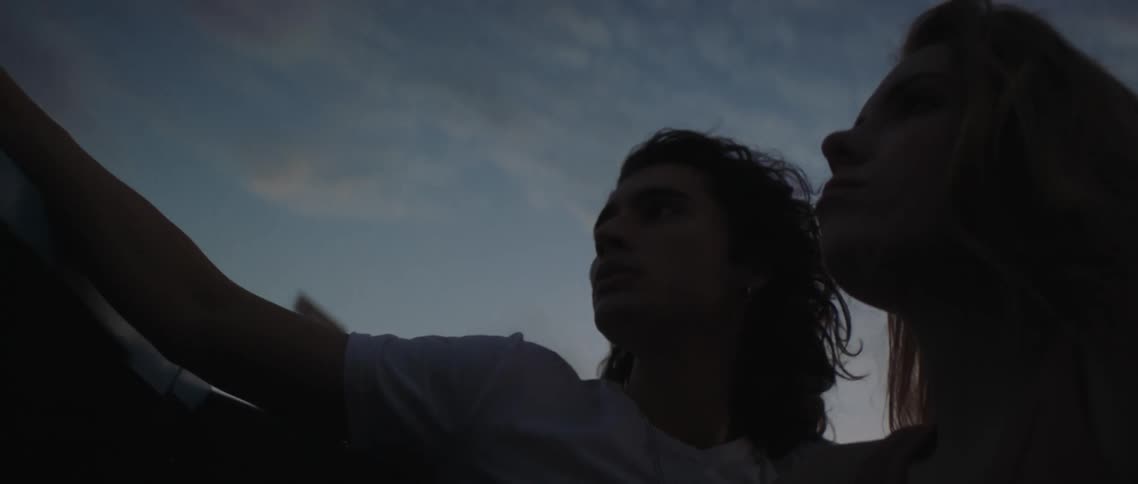 Young couple riding on the back of a car driving on a rural area at sunset
