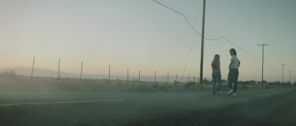 A couple walk down the empty road with dust clouds following behind