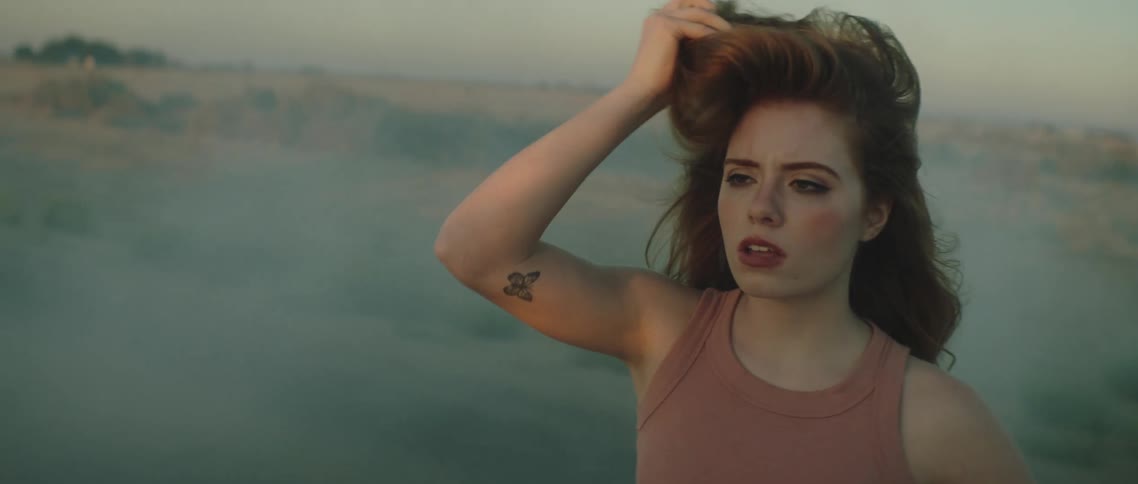 Young woman standing next to a broken smoking car on a rural road at sunset