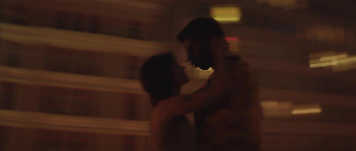 Man and woman holding each other in front of high rise buildings at night