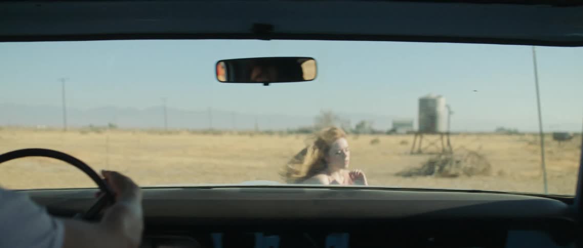 A young woman runs around the front of a vehicle in a rural desert area