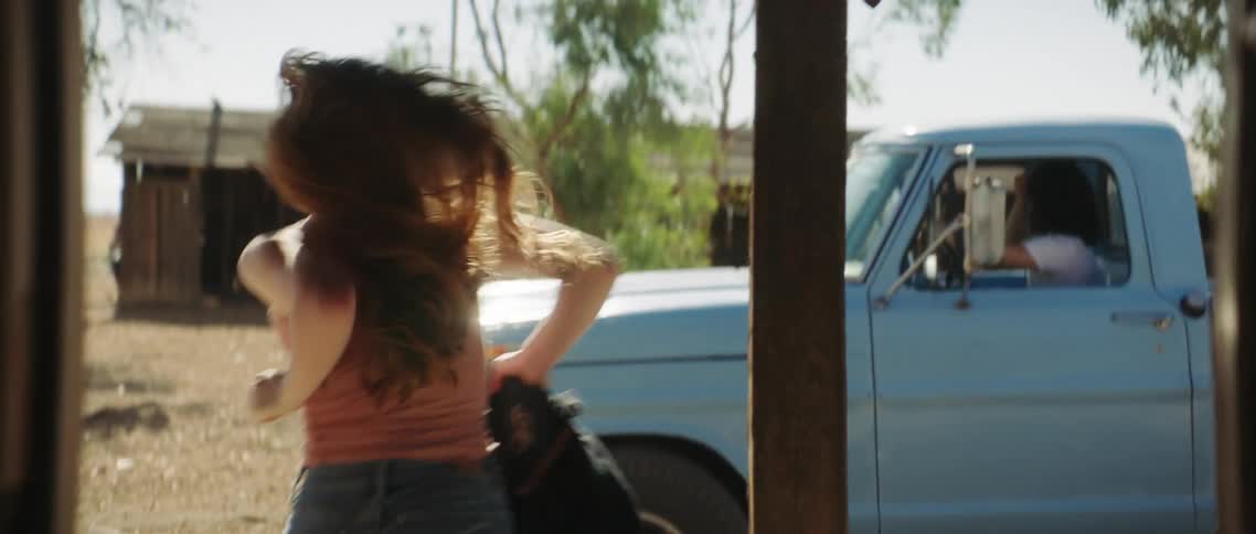 Woman with red hair sleeveless shirt and jeans runs to turquoise pickup truck