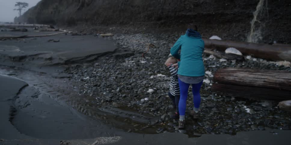 A woman helps her child walk on rocks