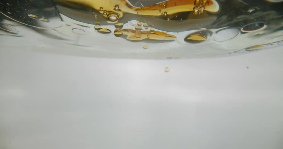 Golden droplets of oil flow into water forming bubbles and floating on the surface