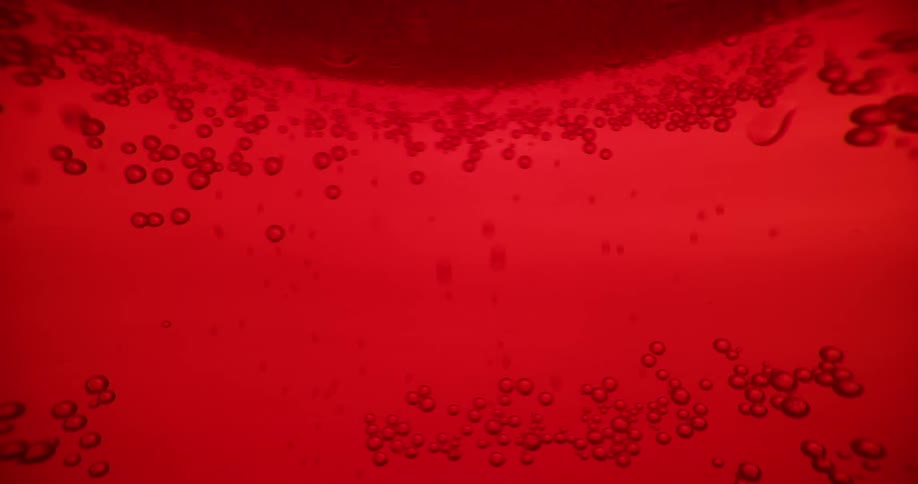 A red liquid is filled with small fizzy bubbles that tend to aggregate together