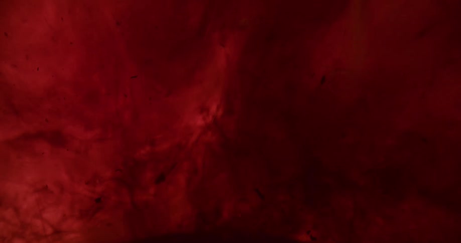 Clusters of dark sediment rise and float in a red liquid