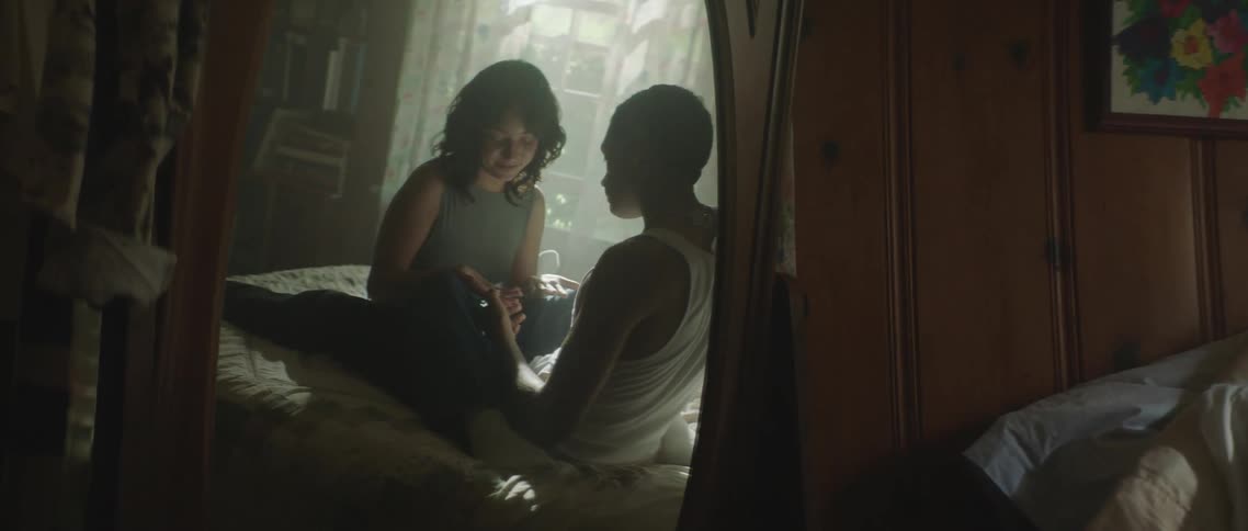 Reflection on a mirror of a young couple sitting on the bed inside a dimly lit room
