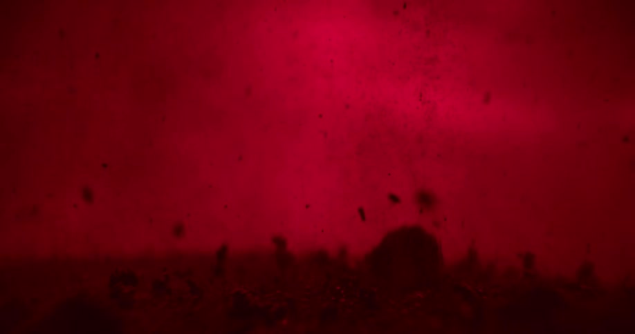 Clusters of sediment float and settle in a red liquid
