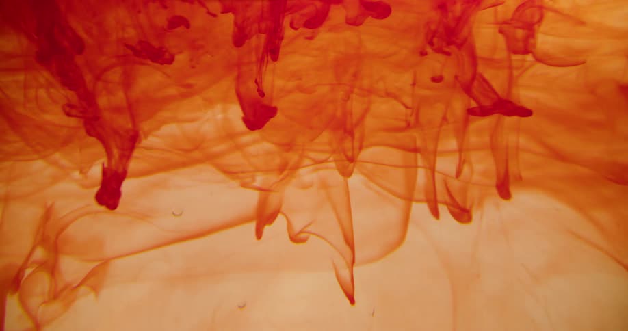 An orange dye spins and spreads in clear liquid