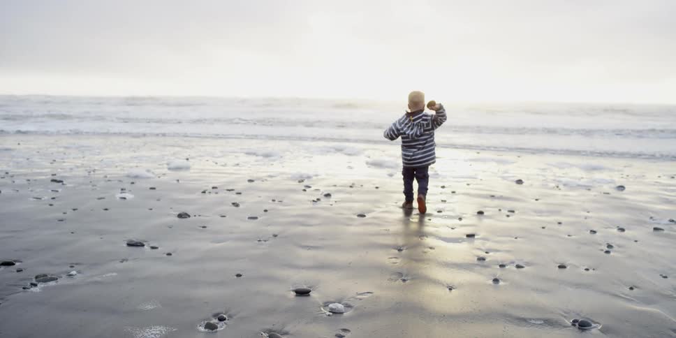 A boy walks on a beach and throws a rock
