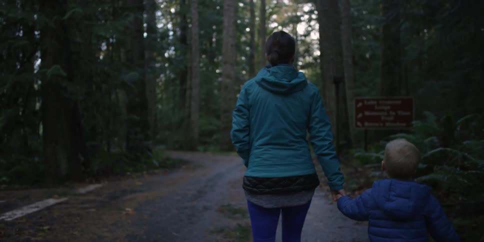 A woman and toddler holding hands as they walk through a forest