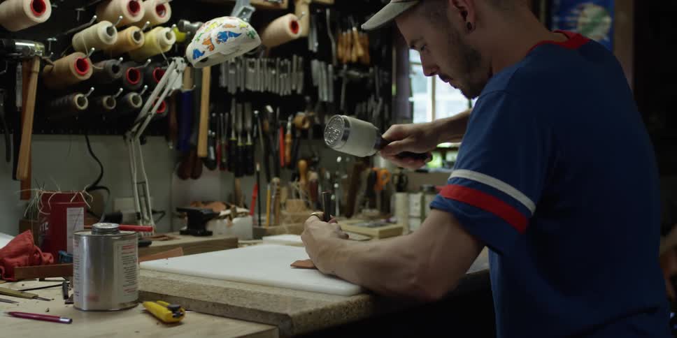 A man grabs a tool to pound a hole in something on a workbench