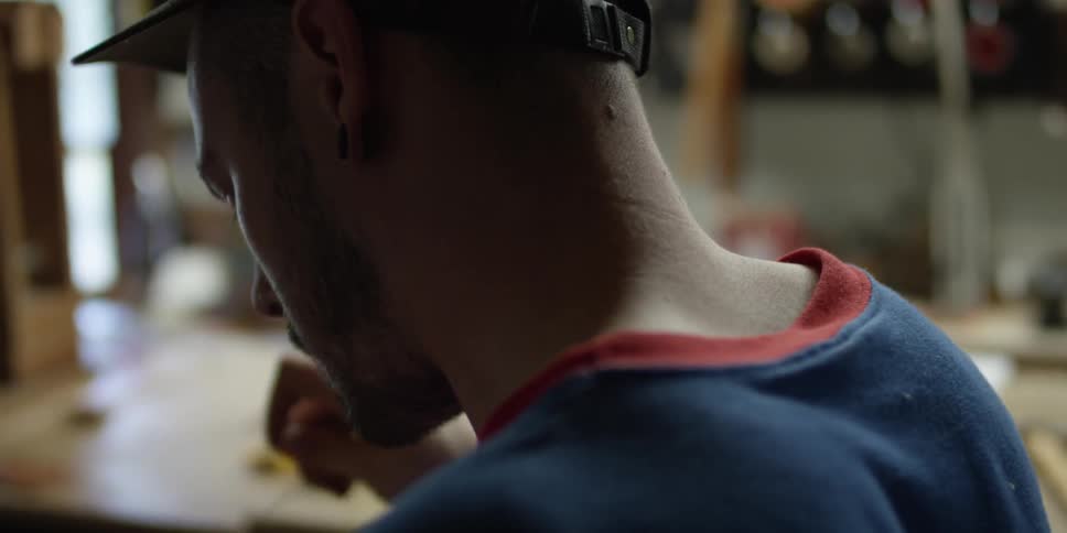 A man in blue threads a needle through a piece of leather