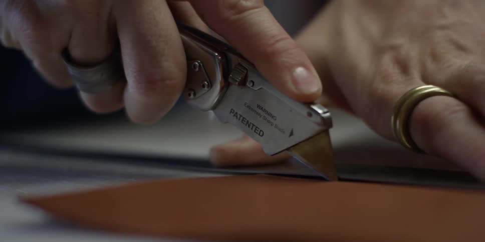 A person cuts a strip of leather with a box cutter