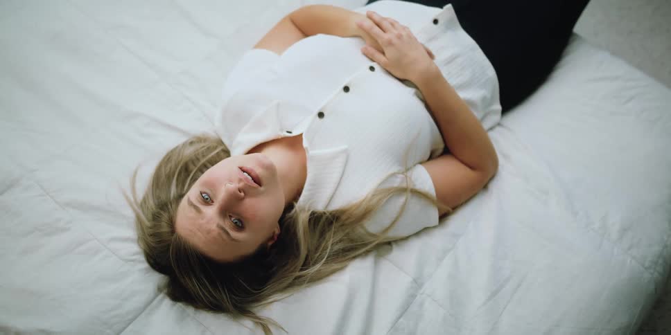 Blonde woman with white shirt and black pants lies down on bed after looking at baby photos