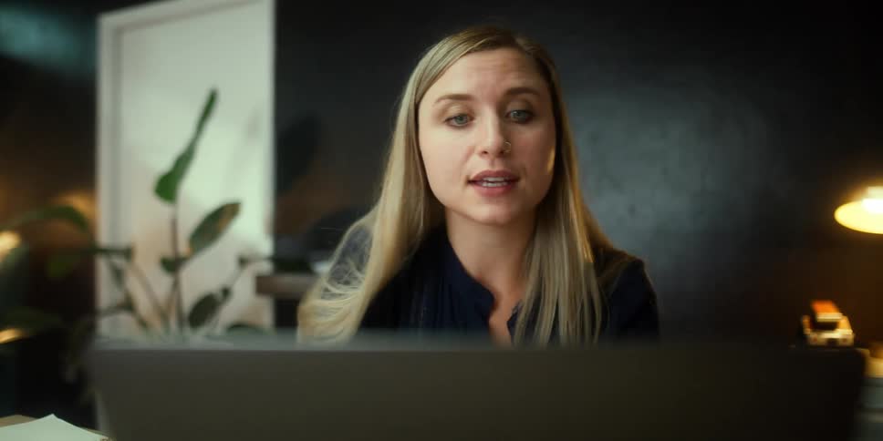 A woman in a room using a laptop with a door a wall and a lamp in the background