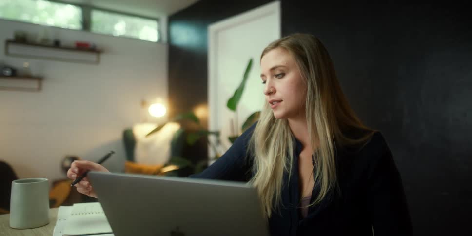 A young woman talking while using a laptop in an office setting