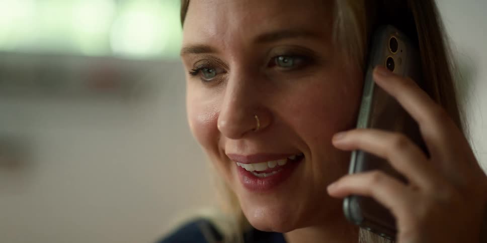Blonde woman with blue eyes and nose ring talks on smartphone smiling