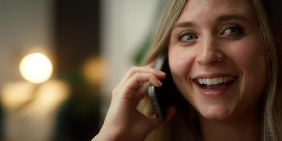 Young blonde woman with a piercing on her nose talking on the phone inside a room