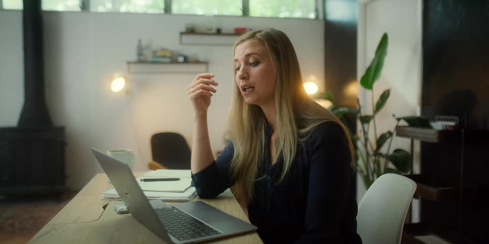A woman is sitting at a desk in front of a laptop talking to someone online