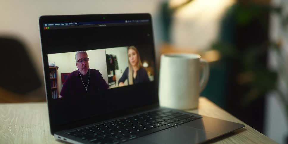 People talking on a video call over a laptop sitting on a desk in the office