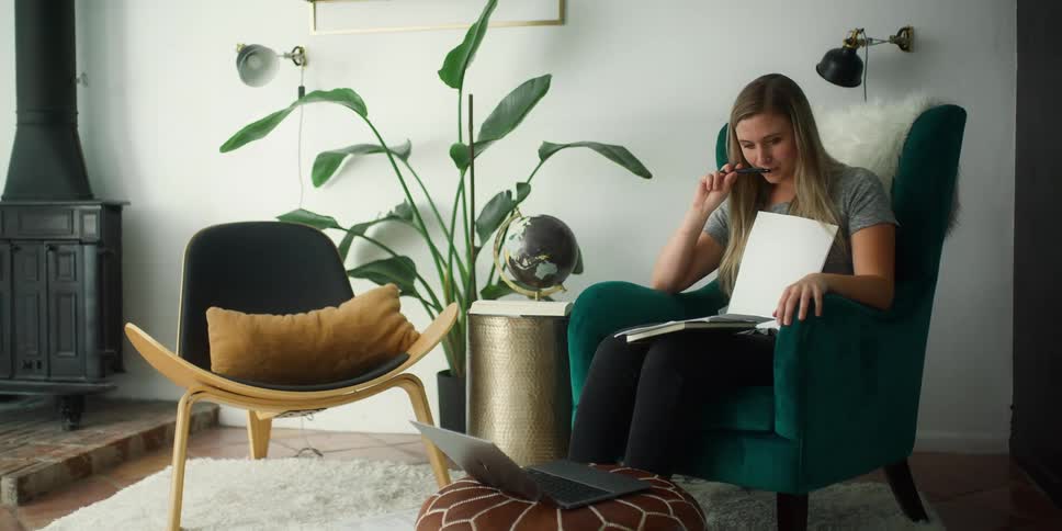 A woman sits in a chair thinking and then writes on a piece of paper