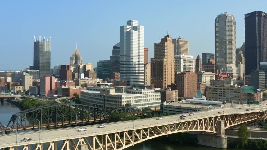Vehicles cross a wide bridge over a river that runs through downtown