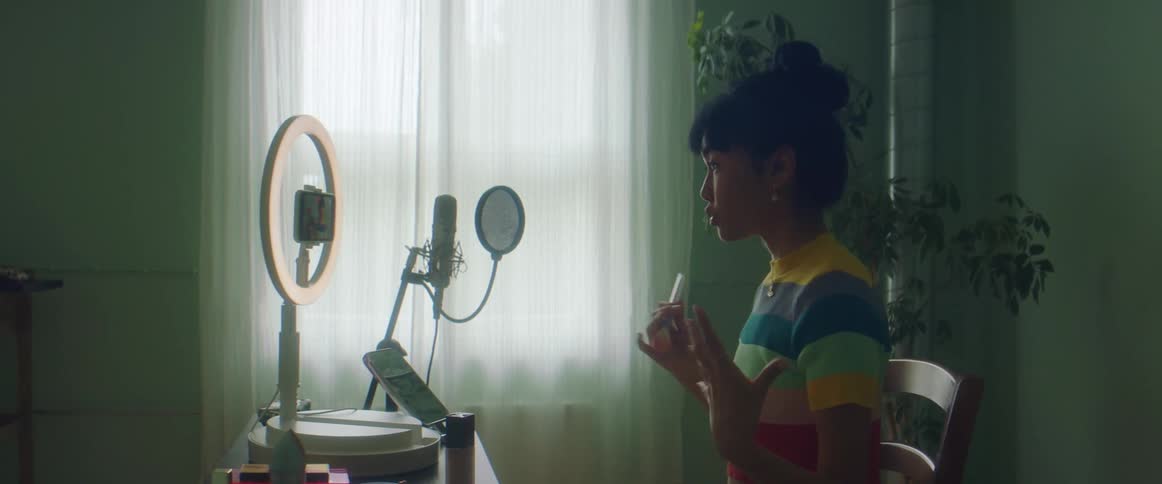 Woman with colorful shirt sits in armchair and talks while filming herself on smartphone