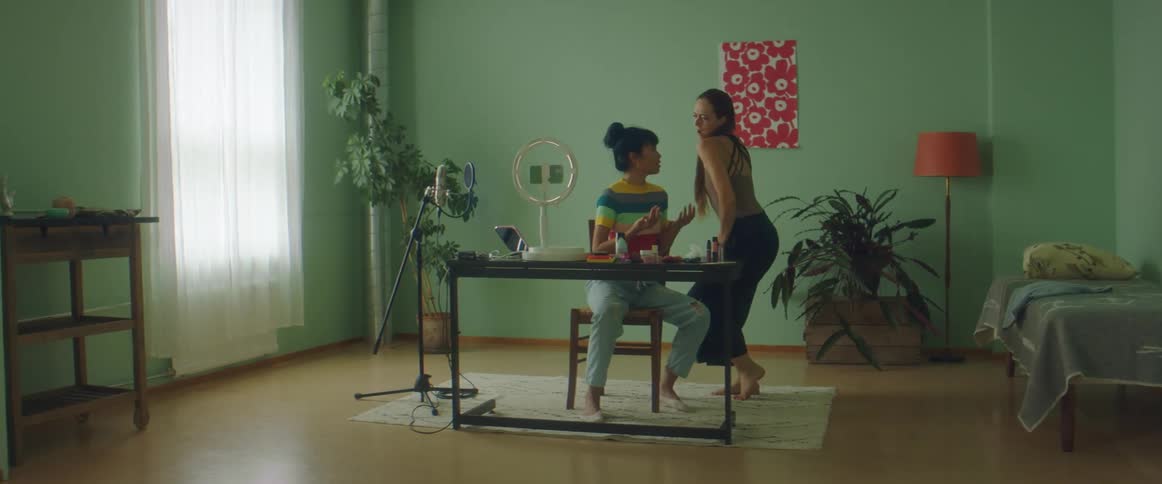 A woman is sitting at a desk when another woman walks in and does a dance