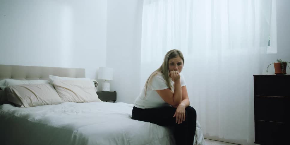 A sad looking woman is sitting on a bed and staring off