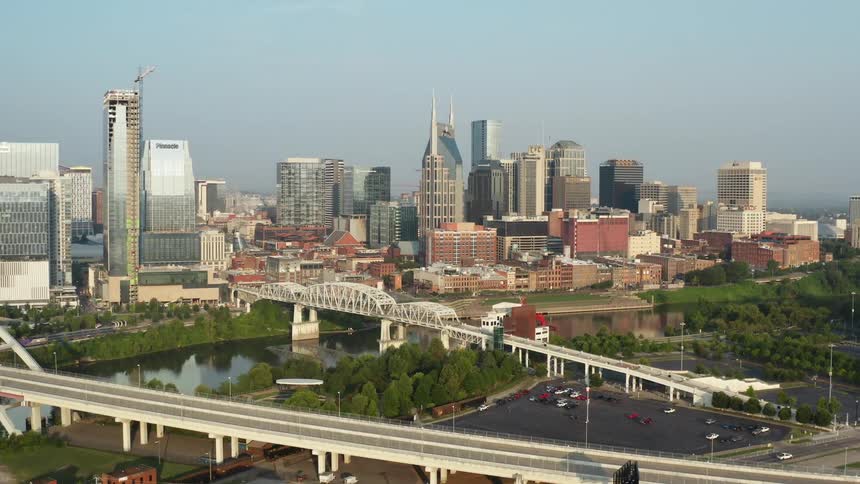 A city skyline with buildings and skyscrapers with a river and bridge with the sky and clouds in the background