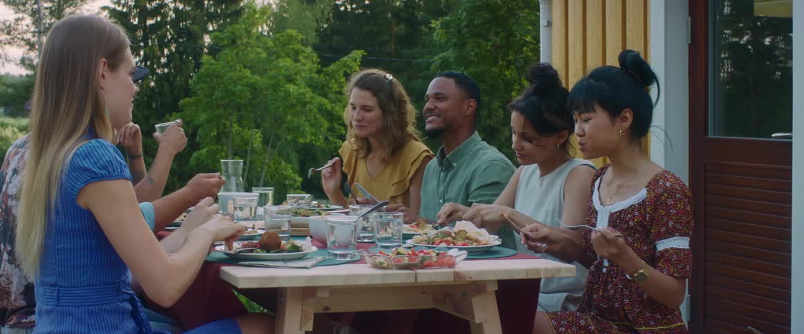 Friends sit outdoors on patio at picnic table eating and talking