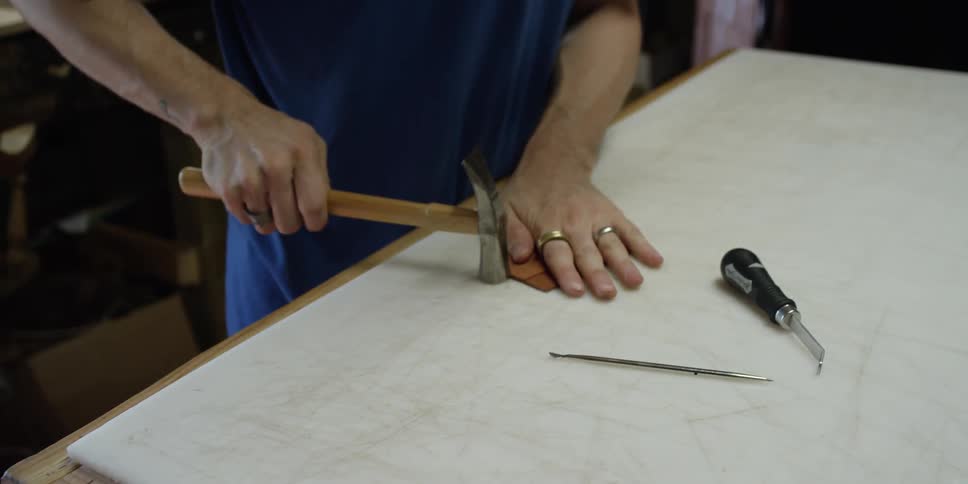 A man bangs a piece of leather with a hammer